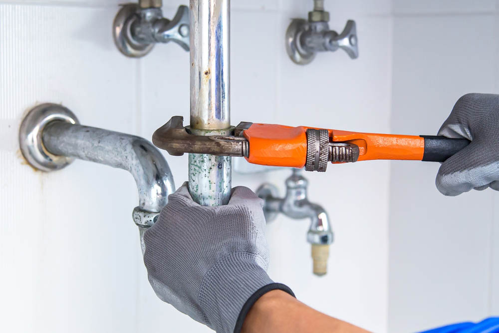 Plumber using a wrench to tighten loose pipe fittings